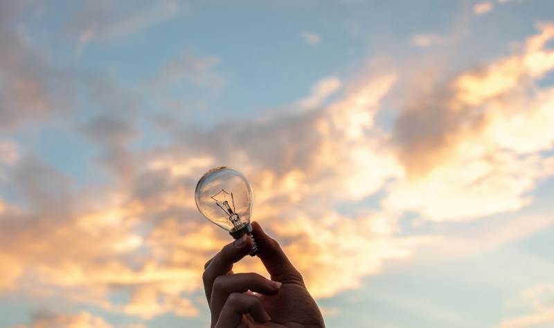 Hand holding a light bulb against a sunset sky.