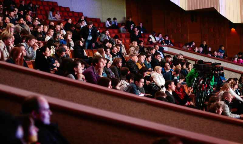 Audience seated in tiered rows watching an event with cameras present.
