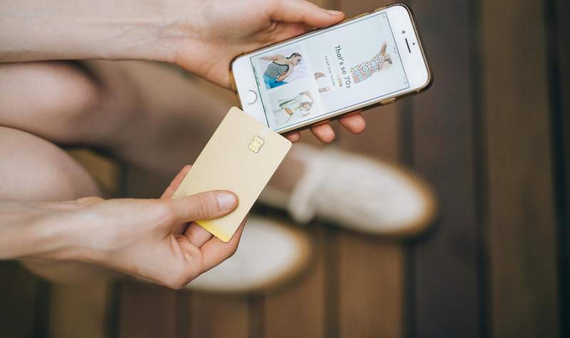 A person holding a smartphone with an online shopping app open and a credit card in hand.