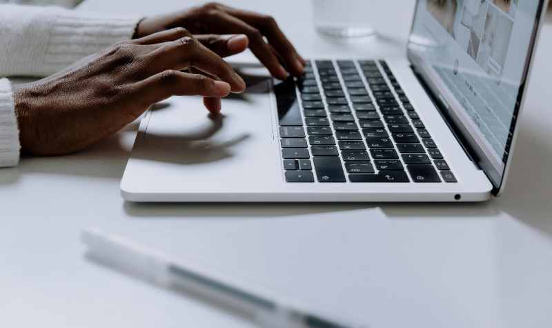 Person typing on a laptop with a pen nearby.