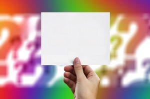 Hand holding blank card with colorful question marks in background.