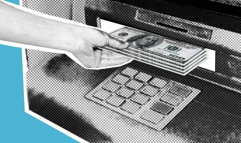 A hand inserts cash into an ATM's deposit slot.