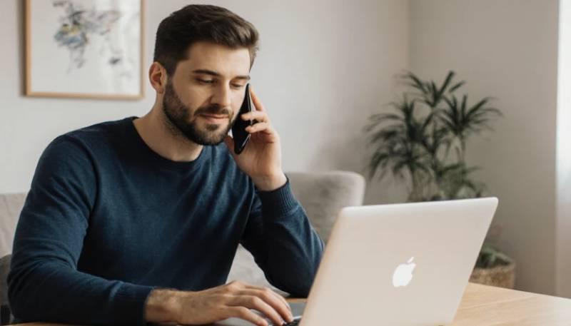 Man working on laptop while talking on phone.