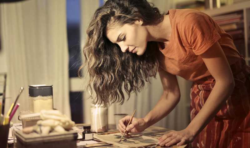 Woman painting at night with art supplies around her.