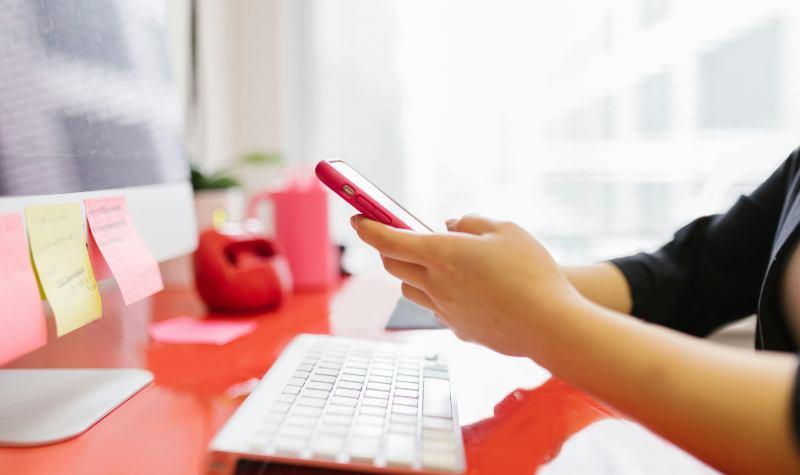 Person using smartphone at desk with keyboard and sticky notes.