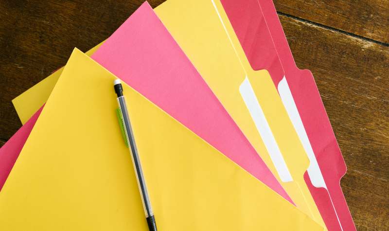 "Colorful folders with pen on wooden surface."