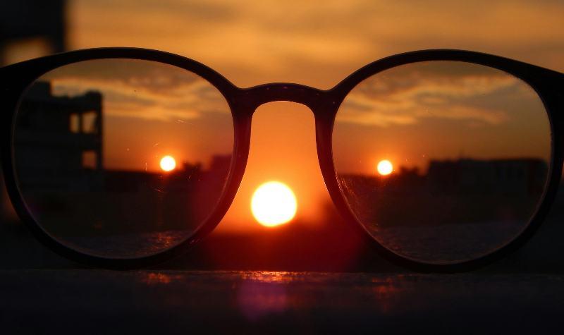 Glasses frame sunset with buildings silhouetted against vibrant sky.