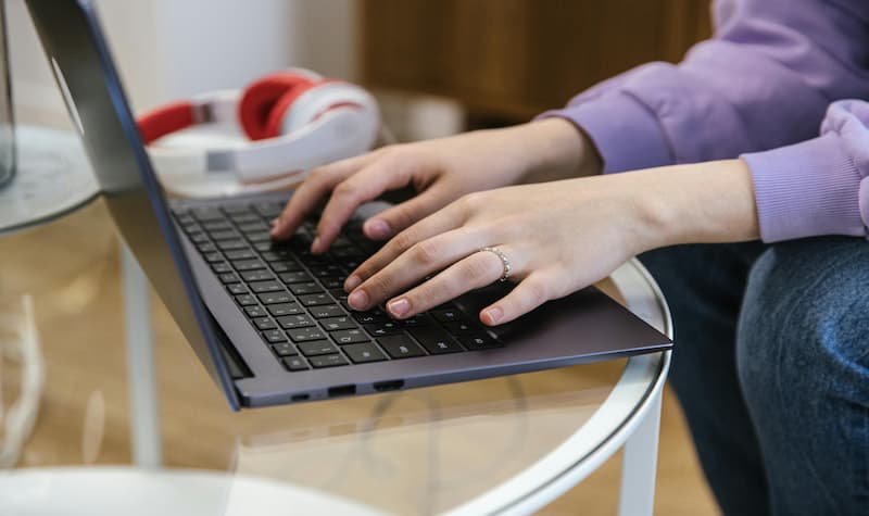 A person typing on a laptop with headphones nearby.