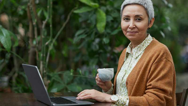 Woman with laptop outdoors, holding cup of tea.