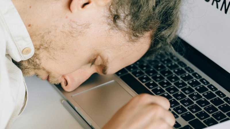 Man resting head on laptop keyboard, eyes closed, possibly tired or overwhelmed.