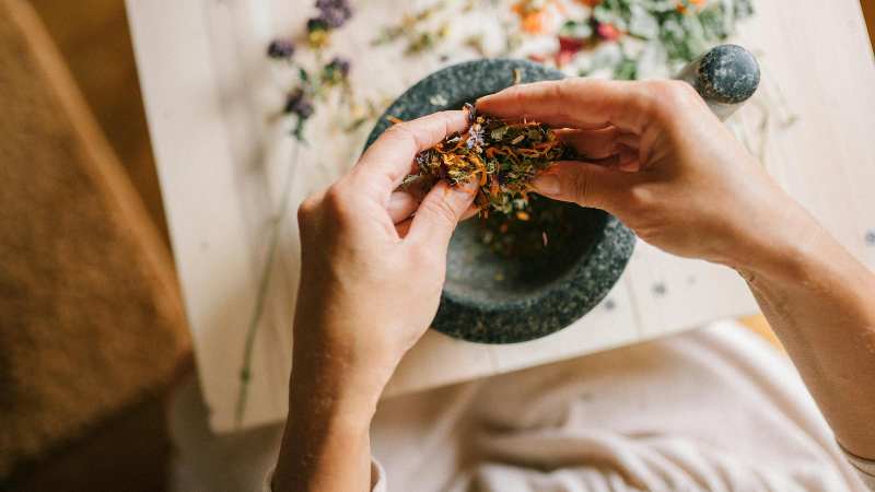 Hands crushing herbs with a mortar and pestle on a table.