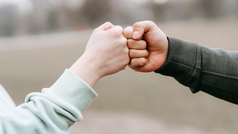 Two hands bumping fists against an outdoor backdrop.