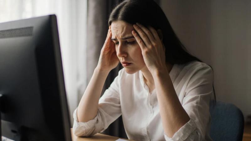 Woman at desk with computer, appears stressed or overwhelmed.