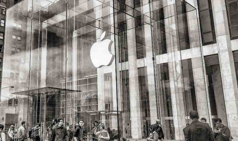 Apple Store with large glass facade and iconic logo, people gathered outside.