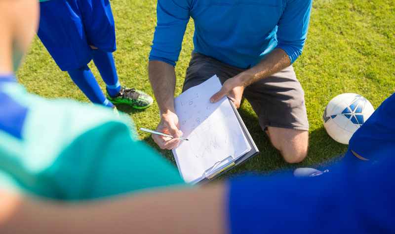 Soccer coach discussing strategy with players on field.