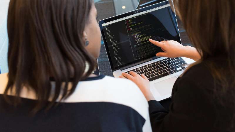 Two women collaborating on coding at a laptop.