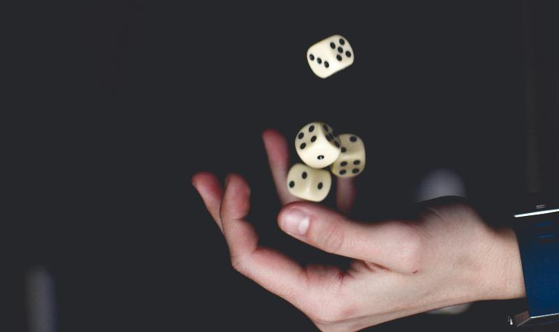 A hand tossing three dice against a dark background.