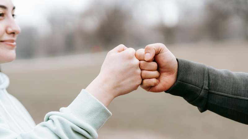 Two people bump fists in an outdoor setting.
