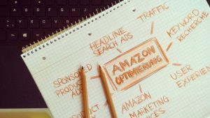 Notepad on a laptop keyboard with "Amazon Optimierung" at the center. Surrounding words include "Headline Search Ads" and "Keyword Recherche" in orange pencil.