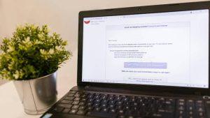Open laptop displaying an email with transactions, beside a small potted plant on a white surface, conveying a modern, workspace setting.