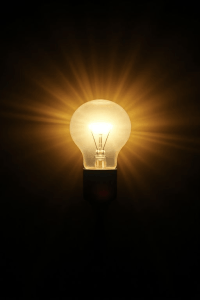 A glowing light bulb shines brightly in the dark, radiating warm, golden rays. The image conveys a sense of illumination and inspiration.