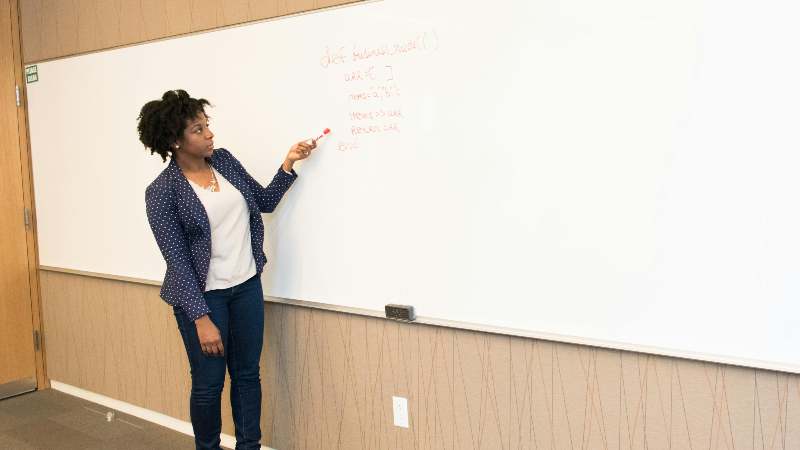 A woman presents at a whiteboard with notes written in red marker.