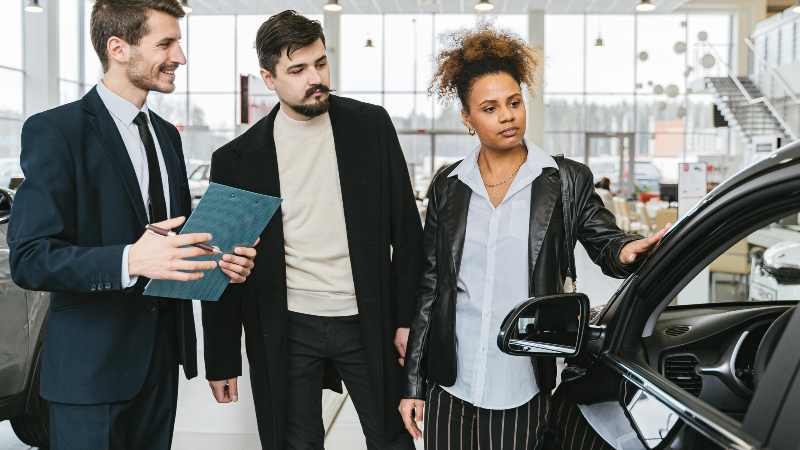 Three people examining a car interior at a showroom.
