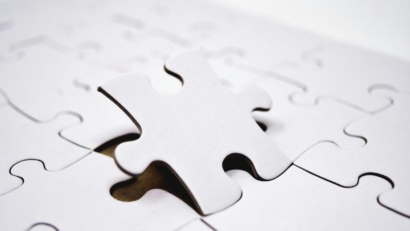 Close-up of a white jigsaw puzzle with one piece raised above its spot, almost completing the puzzle. Conveys a sense of anticipation and problem-solving.